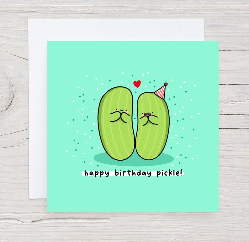 May include: A light green card with two green pickle characters wearing party hats. The card has a red heart and white confetti. The text on the card reads "happy birthday pickle!"