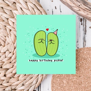 May include: A light green card with two green pickles wearing party hats and smiling at each other. The text "happy birthday pickle!" is written below the pickles.