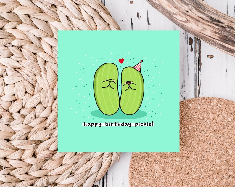 May include: A light green card with two green pickles wearing party hats and smiling at each other. The text "happy birthday pickle!" is written below the pickles.