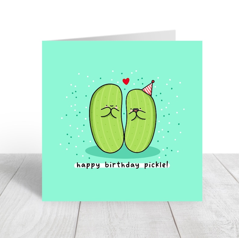 May include: A green birthday card with two cartoon pickles wearing party hats and a red heart above them. The text on the card reads "happy birthday pickle!"