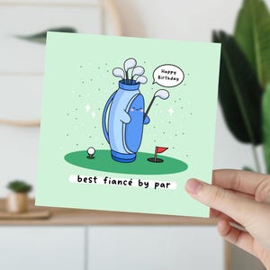 Puede incluir: Tarjeta de felicitaci&oacute;n verde claro con un tema de golf de dibujos animados. La tarjeta presenta una bolsa de golf azul con una cara sonriente, palos de golf, una pelota de golf y una bandera roja. El texto dice "Happy Birthday" y "best fianc&eacute; by par."