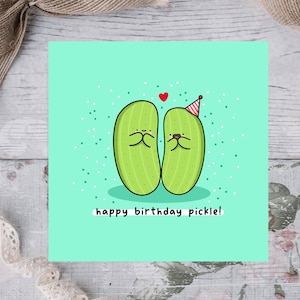 May include: A green birthday card with two cartoon pickles wearing party hats. One pickle is holding its hands over its mouth and the other pickle is smiling. The card says "happy birthday pickle!"