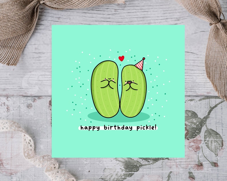 May include: A green birthday card with two cartoon pickles wearing party hats. One pickle is holding its hands over its mouth and the other pickle is smiling. The card says "happy birthday pickle!"