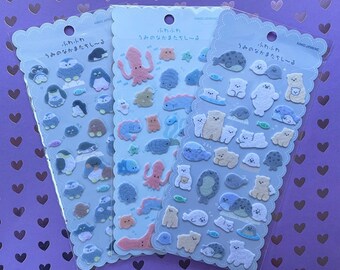 May include: Three sheets of stickers featuring various sea creatures. The stickers are on a light blue background with white outlines. The first sheet features penguins, the second sheet features an octopus, a starfish, and a seahorse, and the third sheet features seals. The stickers are all in Japanese.
