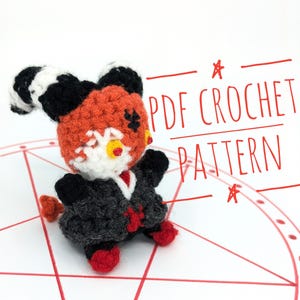 May include: A handmade crochet doll with orange, black, white, and red yarn. The doll has large ears, a dark gray outfit, and red accents. The text "PDF CROCHET PATTERN" is written in red.