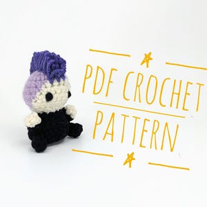 May include: A handmade crochet doll with a purple mohawk, a light purple and cream-coloured head, and a black body. The doll is sitting on a white surface. The text "PDF CROCHET PATTERN" is written in yellow.