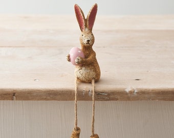 Sitting bunny rabbit holding pink Easter egg with dangling legs