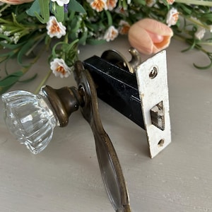 May include: Antique brass door knob with a clear glass knob and a matching backplate. The door knob has a simple design and is in good condition.