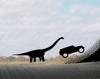 May include: Black silhouette sticker featuring a Brontosaurus dinosaur and a Jeep. The dinosaur is walking, and the Jeep is tilted. The background shows a sky and trees. The sticker is likely for a car window.
