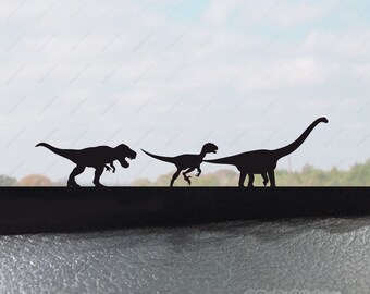 May include: Three black silhouette dinosaur decals, a Tyrannosaurus Rex, a Velociraptor, and a Brachiosaurus, on a car window. The decals are arranged in a line, with the Tyrannosaurus Rex on the left, the Velociraptor in the middle, and the Brachiosaurus on the right. The decals are all facing the right. The text "@GoGoStickers" is visible in the lower right corner of the image.