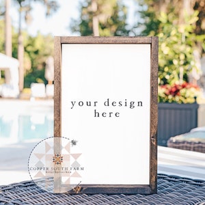 Op de afbeelding: Een wit bord met een bruin houten frame, dat op een rieten stoel staat. Het bord heeft de tekst "your design here".