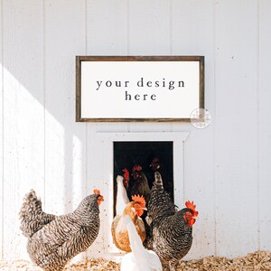 May include: A white wooden sign with a brown frame hanging on a white wooden wall. The sign says "your design here". There are chickens in the background.