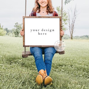 May include: A woman sitting on a swing holding a wooden frame with a white background. The frame has the text "your design here" written on it.