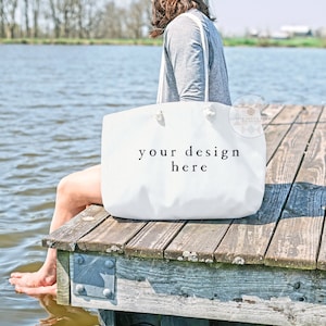 May include: A white canvas tote bag with the text "your design here" on a wooden jetty by a lake.