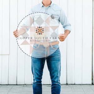 Könnte beinhalten: Eine Person trägt ein hellblaues Jeanshemd und eine blaue Jeans und hält ein rundes Schild mit dem Text "COPPER SOUTH FARM hive-horse-hen" in einem Kreis mit einem geometrischen Muster.