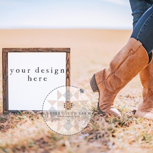 Puede incluir: Un marco de madera con fondo blanco y el texto "your design here". El marco está sentado en un campo de hierba seca con un par de botas de vaquero marrones en primer plano. El texto "COPPER SOUTH FARM" es visible en la esquina inferior derecha de la imagen.