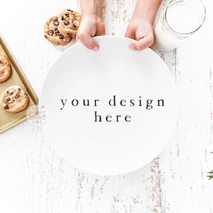 Może przedstawiać: Biały talerz z tekstem "your design here" na nim, trzymany przez dwie ręce. Talerz znajduje się na białym drewnianym stole z tacą ciasteczek z kawałkami czekolady i szklanym słoikiem z mlekiem w tle.