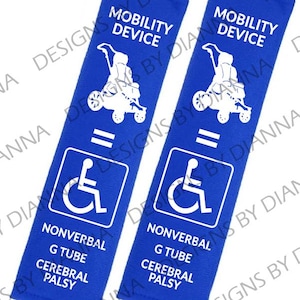 May include: Two blue mobility device straps with white text and graphics. Each strap has the words "MOBILITY DEVICE" at the top, a wheelchair symbol, and the words "NONVERBAL, G TUBE, CEREBRAL PALSY" at the bottom.