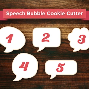 May include: Five white speech bubble cookie cutters with red numbers 1 through 5. The cookie cutters are on a brown wooden surface.
