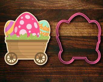 May include: A pink, brown and blue cookie cutter shaped like a wagon with Easter eggs inside. The wagon has two wheels and a wooden bed. The eggs are decorated with polka dots and stripes.