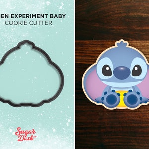 May include: A black cookie cutter shaped like a cartoon character, with a full-colour image of the character beside it. The text "ALIEN EXPERIMENT BABY COOKIE CUTTER" is at the top. The logo "Sugar Dash" is at the bottom.