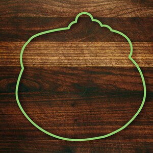 Puede incluir: Un contorno verde de una olla con tapa sobre una superficie de madera marr&oacute;n oscura.