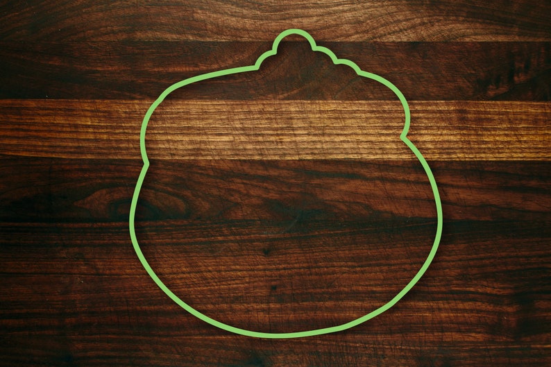 Puede incluir: Un contorno verde de una olla con tapa sobre una superficie de madera marr&oacute;n oscura.