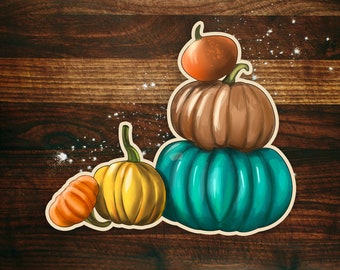May include: A stack of four pumpkins on a wooden background. The pumpkins are different sizes and colors, including orange, brown, yellow, and teal.