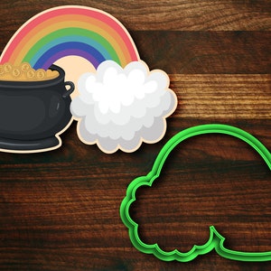 May include: A green cookie cutter shaped like a pot of gold at the end of a rainbow. The rainbow is multi-colored and has a white cloud.