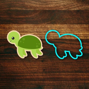 May include: A green turtle cookie cutter with a blue outline. The cookie cutter is on a dark brown wooden surface.