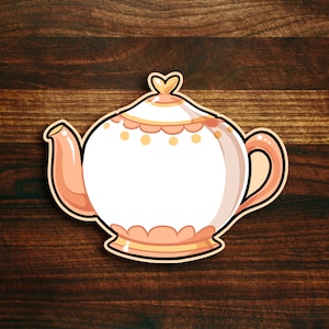 May include: A white teapot with a peach-colored handle and spout. The teapot has a gold trim and a heart-shaped knob on the lid. The teapot is on a brown wooden background.
