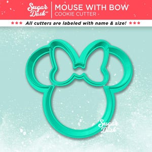 May include: A teal-colored cookie cutter in the shape of a mouse head with a bow. The cutter is made of plastic and has the words "MOUSE WITH BOW COOKIE CUTTER" printed on the top. The text "All cutters are labeled with name & size!" is also visible.