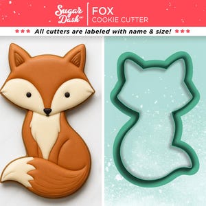 May include: A decorated fox-shaped cookie next to a teal-colored fox cookie cutter. The cookie is brown, white, and black. The cookie cutter is teal. The text "Sugar Dash" and "FOX COOKIE CUTTER" are visible.