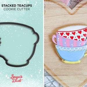 May include: Stacked teacup cookie cutter. The cutter is shaped like three teacups stacked on top of each other. The cutter is black and the background is light blue with white speckles. The text "STACKED TEACUPS COOKIE CUTTER" is at the top of the image. The text "Sugar Dash" is at the bottom of the image.