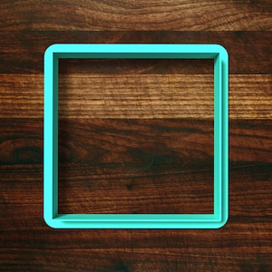 May include: A turquoise blue square-shaped cookie cutter on a brown wooden surface.