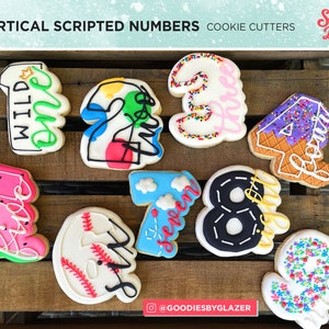 May include: Vertical scripted number cookie cutters for a birthday party. The numbers are decorated with various themes, including wild one, ice cream, watermelon, baseball, and more. The cutters are made by Sugar Dash.