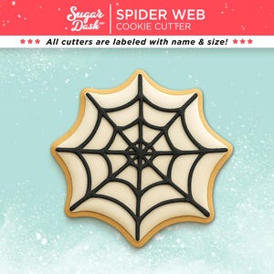May include: A spider web cookie cutter with a black web design on a light-colored cookie. The cookie has a light brown border and is set against a light blue background. The text "SPIDER WEB COOKIE CUTTER" is at the top.
