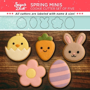 May include: Set of five spring-themed cookie cutters. The cutters are shaped like a chick in an egg, a carrot, a bunny, a flower, and an egg with stripes. The cutters are made of metal and are labeled with their name and size.