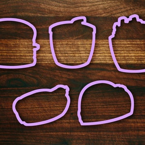 May include: Five purple cookie cutters on a brown wooden surface. The cutters are shaped like a burger, a cup, a cupcake, a lemon, and a heart.