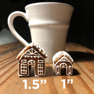 May include: Two gingerbread houses, one 1.5 inches tall and the other 1 inch tall, on a wooden surface next to a white ceramic mug.