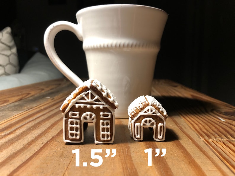 May include: Two gingerbread houses, one 1.5 inches tall and the other 1 inch tall, on a wooden surface next to a white ceramic mug.