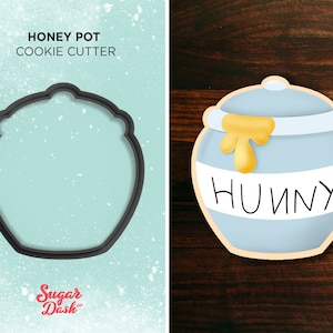 May include: A blue cookie cutter shaped like a honey pot with the word "HONEY" written on it. The cookie cutter is on a wooden background.