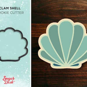 May include: A clam shell cookie cutter, a kitchen tool for baking, is shown on a light blue background with the text "CLAM SHELL COOKIE CUTTER" and the logo "Sugar Dash". The cookie cutter is also shown on a wooden surface.