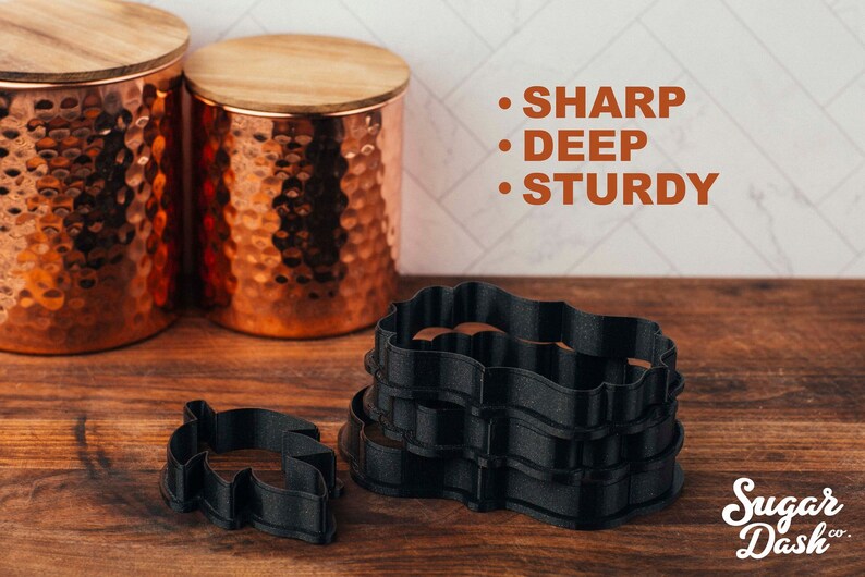 May include: A set of four black cookie cutters, featuring a wavy, ornate design. The cutters are stacked on top of each other. The text "SHARP", "DEEP", and "STURDY" is written in orange on a white background. The text "Sugar Dash co." is written in white on a black background.
