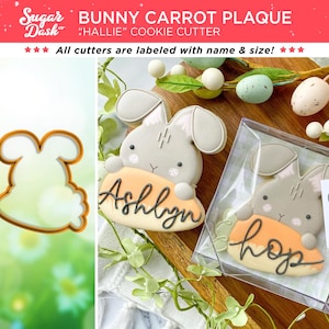 May include: A cookie cutter in the shape of a bunny holding a carrot. The cutter is labeled "Hallie" and is part of a bunny carrot plaque cookie cutter set. The image also shows two decorated cookies, one with the name "Ashlyn" and the other with the word "Hop".