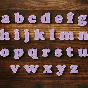 May include: Purple alphabet letters on a brown wooden background.