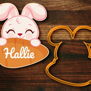 May include: A pink bunny rabbit cookie cutter with a carrot in its mouth. The carrot has the name "Hallie" written on it. There is also a blank bunny cookie cutter.