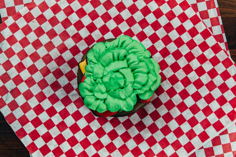 Puede incluir: Una galleta glaseada verde y roja con forma de hamburguesa sobre un papel de cuadros rojos y blancos.