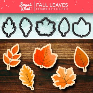 May include: A set of six cookie cutters shaped like fall leaves. The cutters are made of metal and have a silver finish. The cutters are arranged in a row on a wooden surface. The cutters are labeled "Fall Leaves Cookie Cutter Set".
