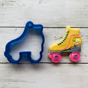 May include: A blue plastic roller skate cookie cutter and a yellow decorated roller skate cookie with pink wheels.